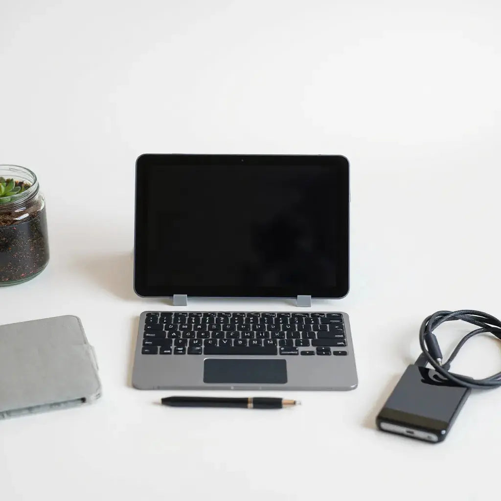 Tablet on a stand with a case, keyboard, stylus, and charging cable arranged neatly nearby